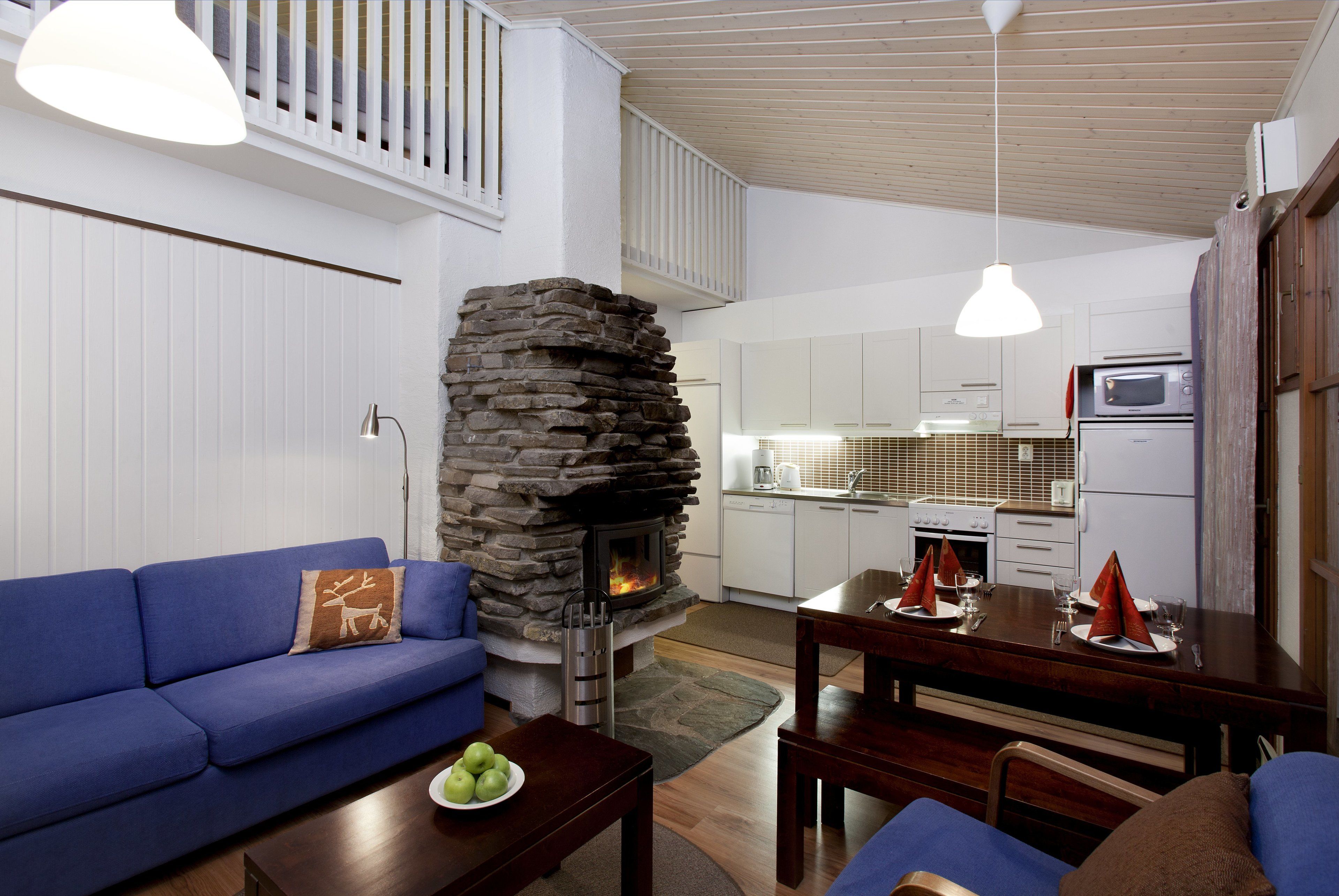 A modern living room with a stone fireplace, a blue sofa, and a dining area with a wooden table set for a meal.