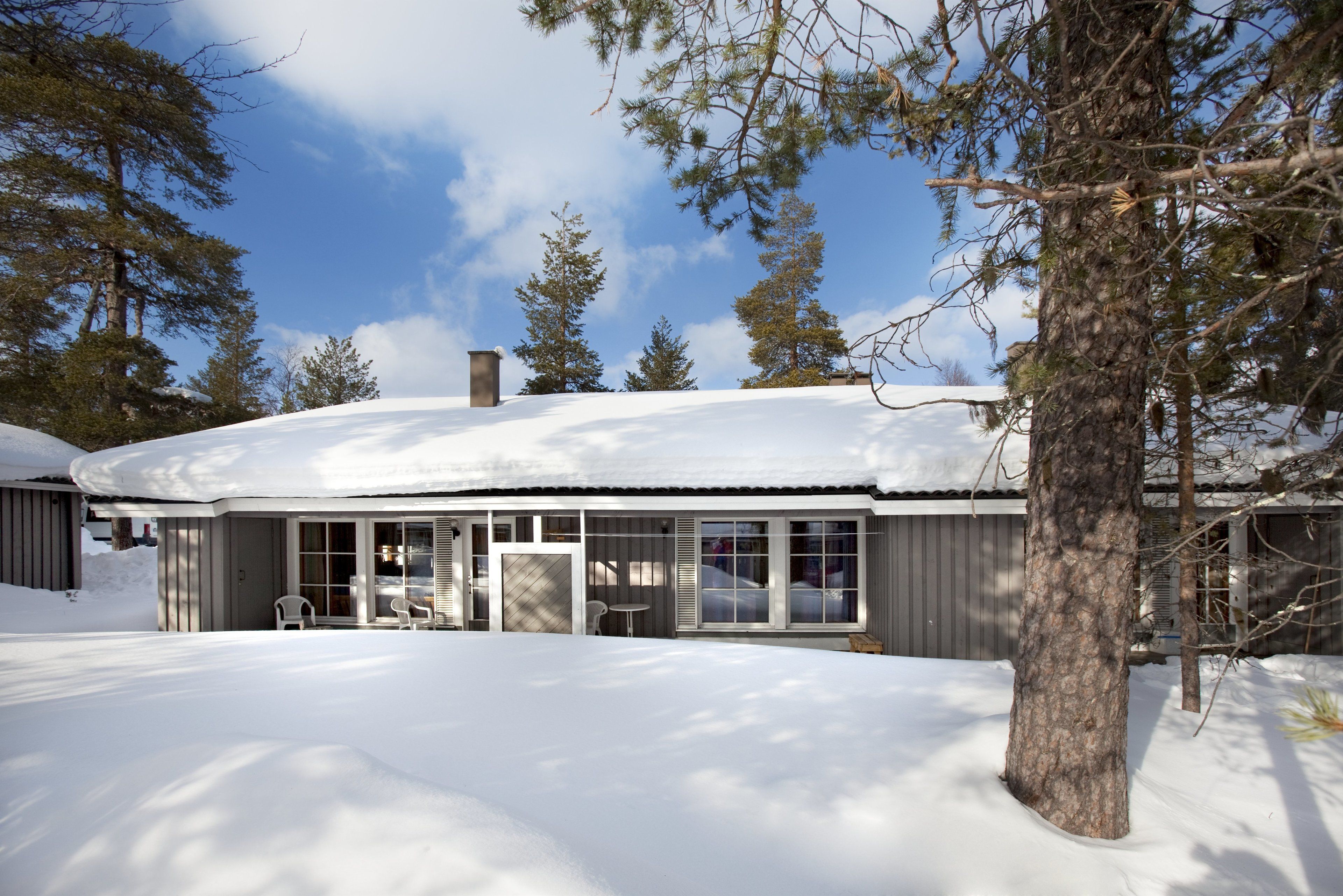 Una casa cubierta de nieve con un patio, ventanas grandes y una chimenea.