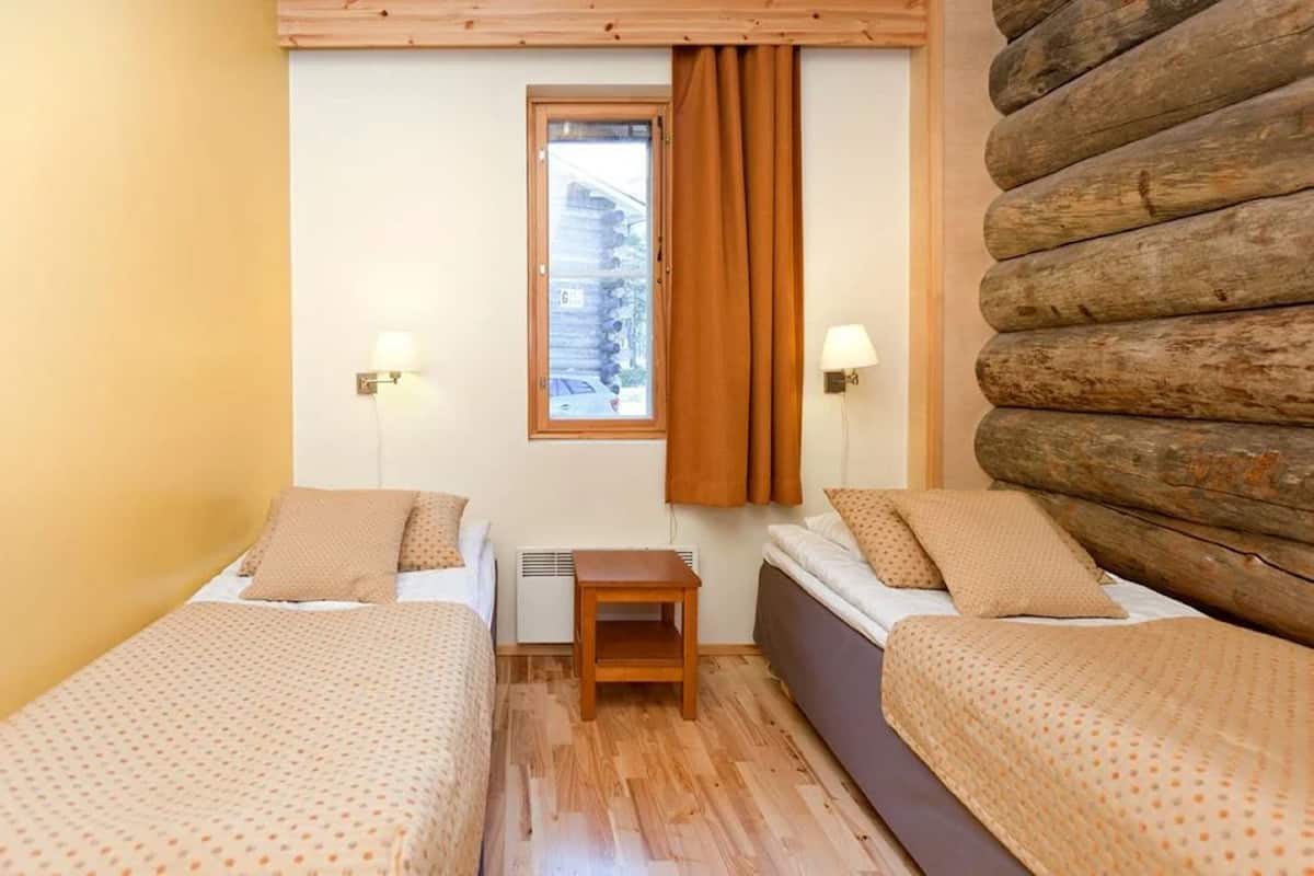 A cozy room with two beds, a small table, and a window with curtains.