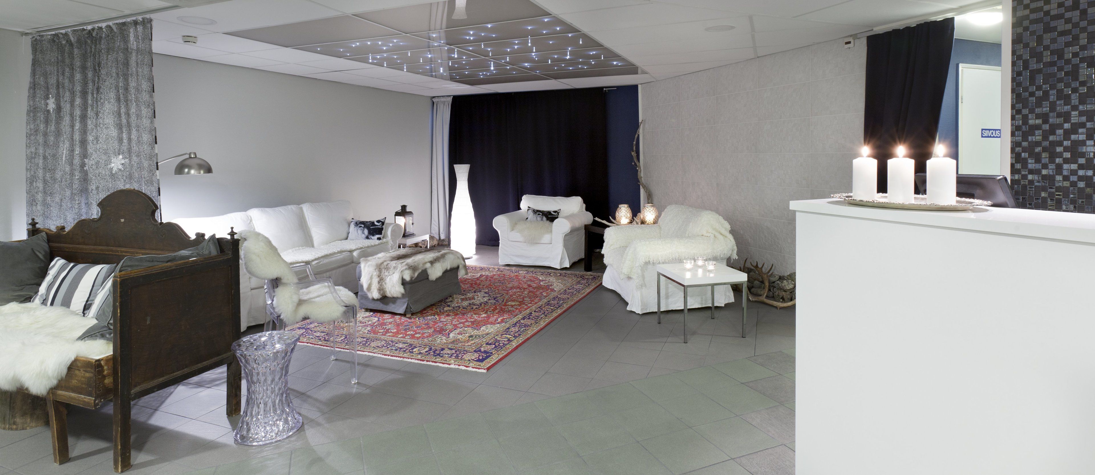 Un salon moderne avec un lit en bois, des canapés blancs, une table basse en verre et un tapis à motifs.