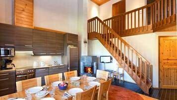 A modern kitchen with dark cabinets, a dining area with a wooden table set for four, and a wooden staircase leading to an upper level.