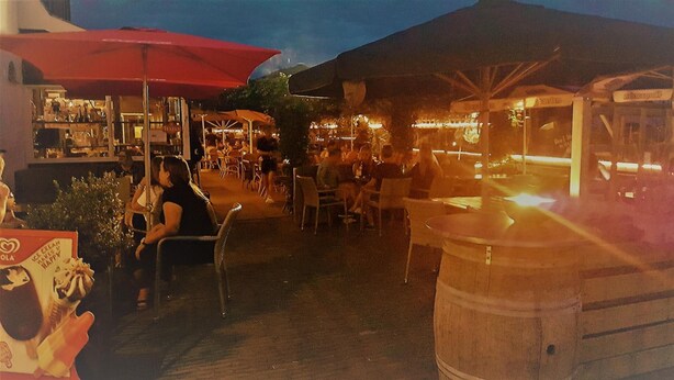 Un área de comedor al aire libre con mesas y sillas, un paraguas rojo y un puesto de comida.