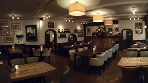 Un restaurante con varias mesas y sillas, suelo de madera y lámparas colgantes.