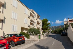 A street view with a row of beige multi-story buildings, parked cars, and a clear blue sky.