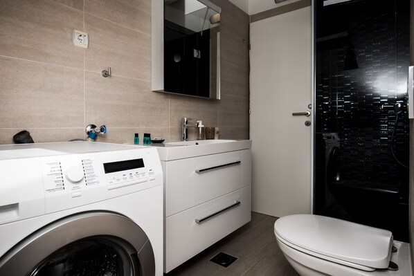 A modern bathroom with a washing machine, a sink, and a toilet.