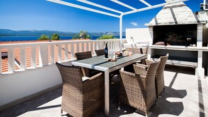A terrace with a table and chairs, a stone oven, and a view of the sea. - Mazuranic Apartments (Bol)