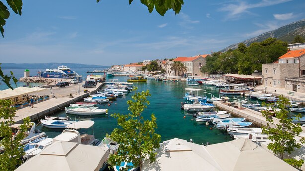 A marina with numerous boats docked, surrounded by buildings with red roofs and a clear blue sky. - Mazuranic Apartments (Bol)