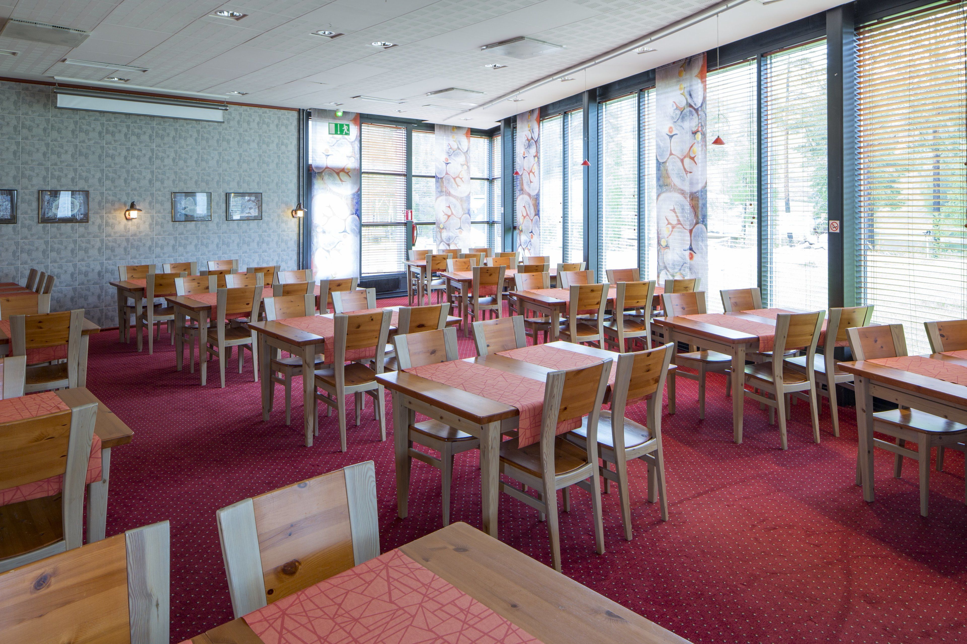 Une salle de conférence dotée de plusieurs tables et chaises, de grandes fenêtres équipées de stores et d’un sol recouvert d’une moquette rouge.
