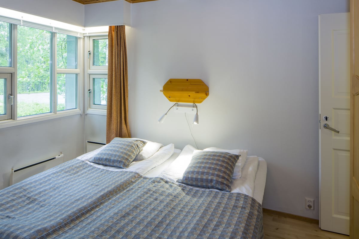 A bedroom with a bed, two pillows, a wooden shelf, and a window with curtains.