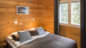 Een kamer met houten lambrisering, een bed, twee bedlampen en een raam met gordijnen.
