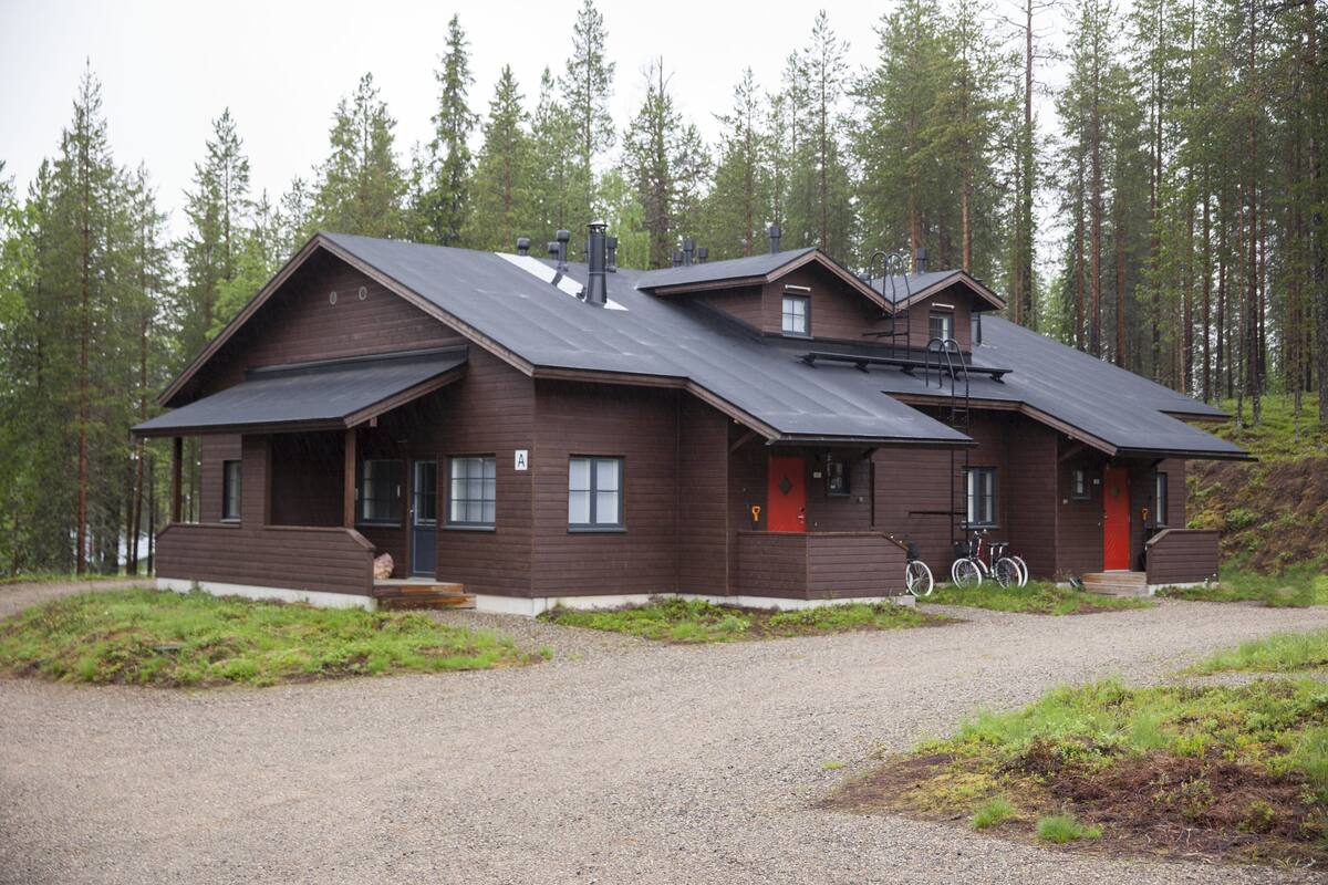 A cabin with a sloped roof, a front porch, and a red door.