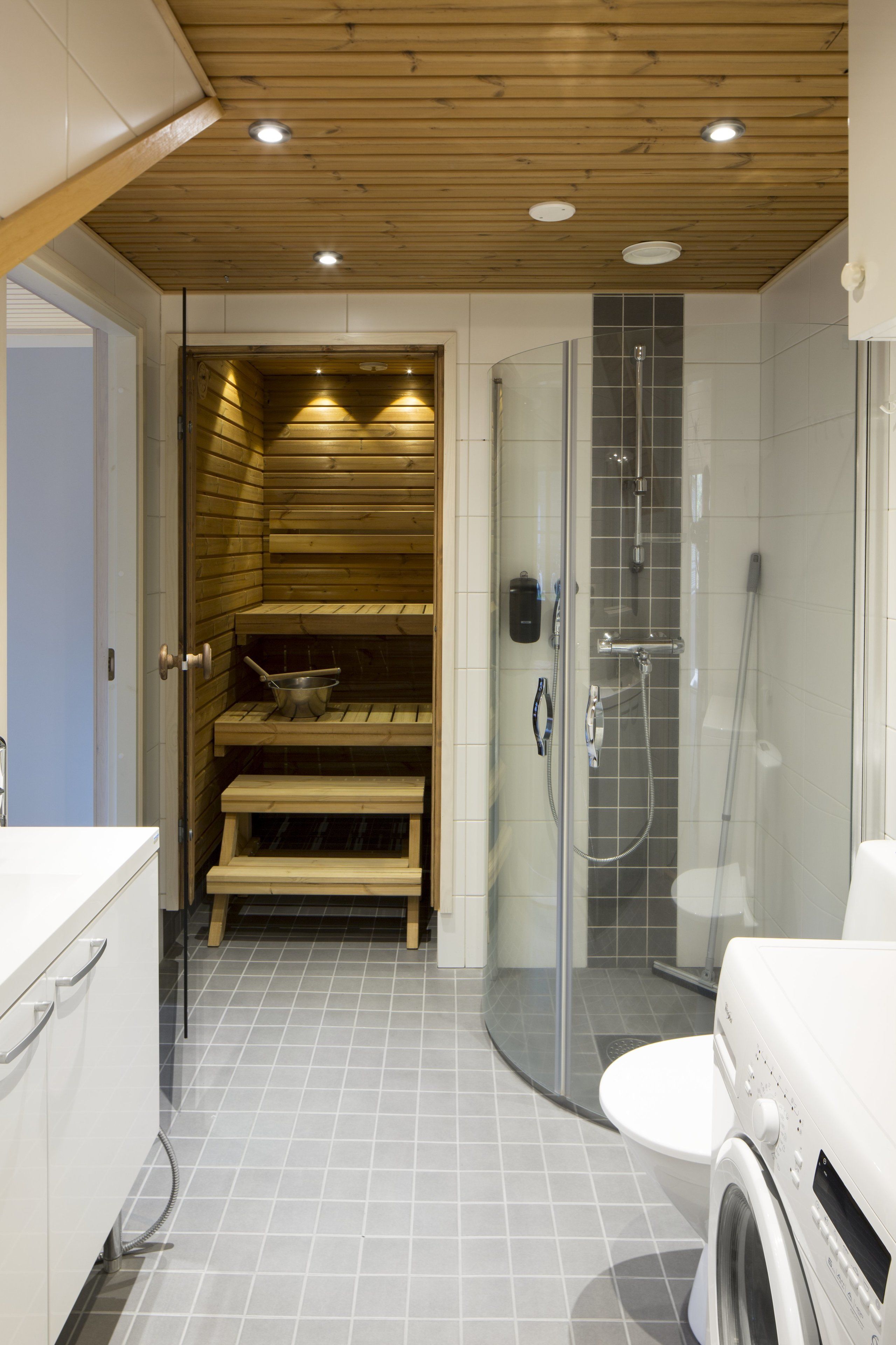 A modern bathroom with a wooden sauna, a glass-enclosed shower, and a washing machine.
