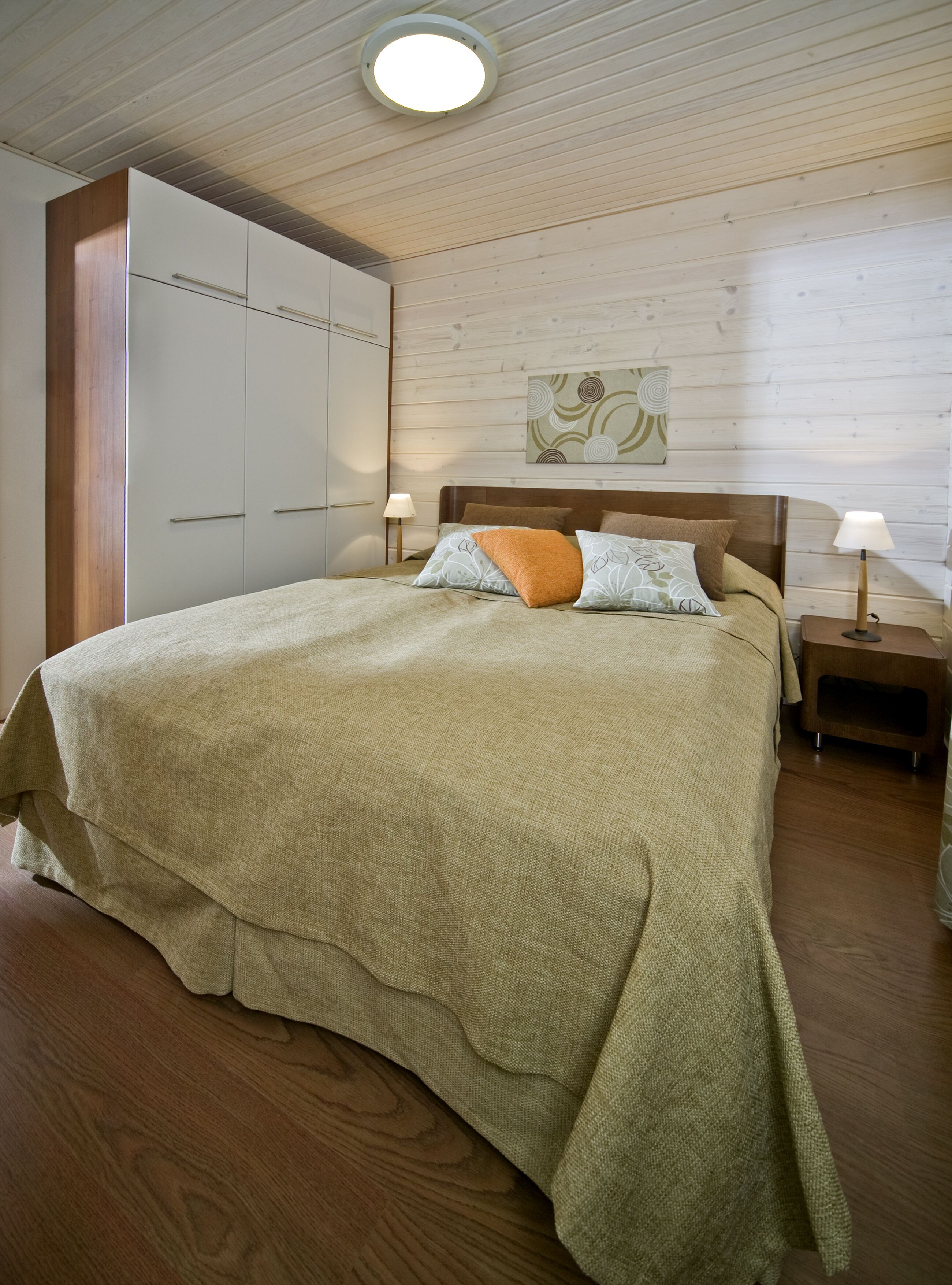 Une chambre à coucher comprenant un lit, des tables de chevet, une armoire et un luminaire au plafond.