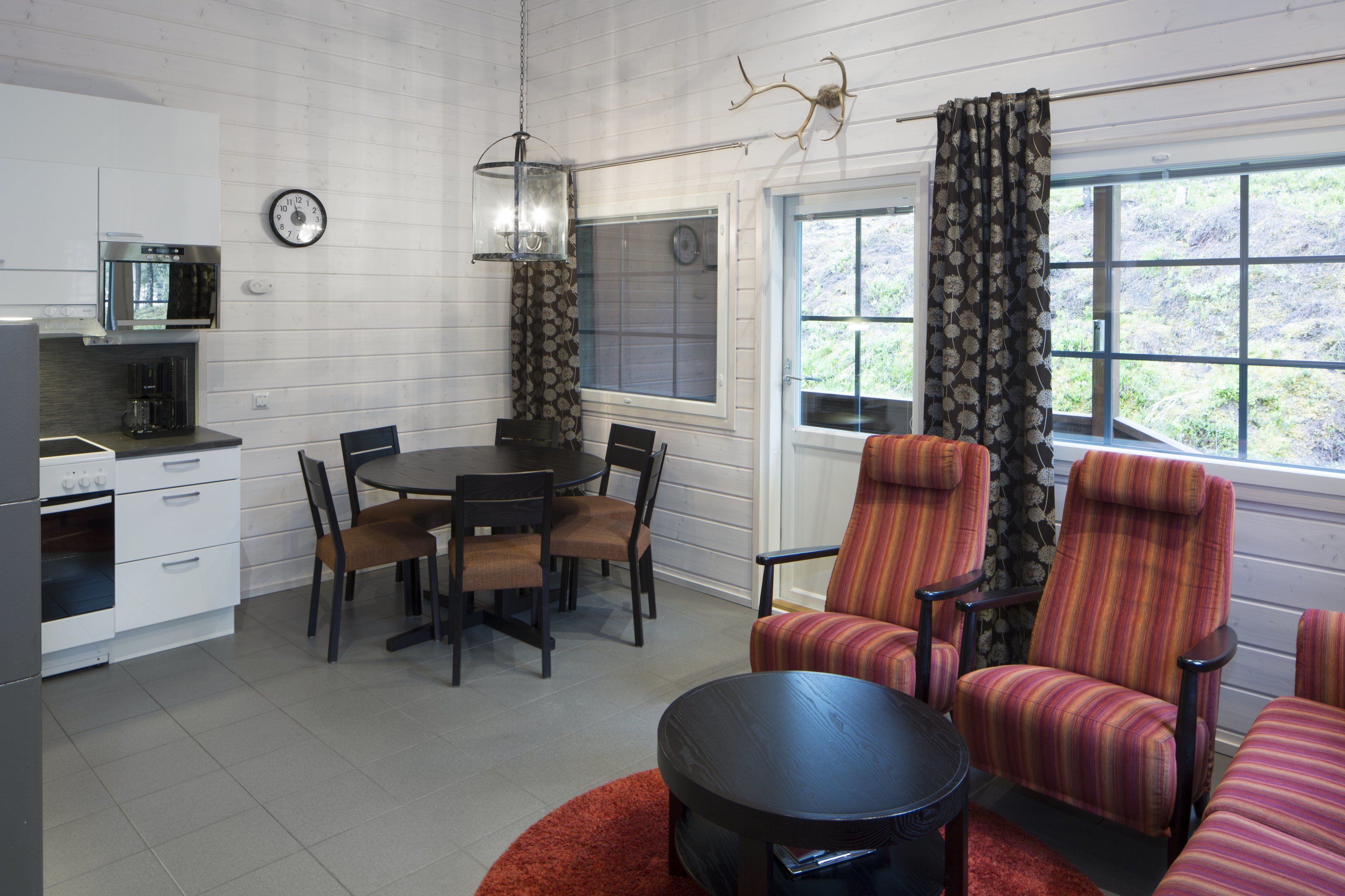 A compact kitchen with modern appliances, a dining area with a round table and chairs, and a cozy seating area with striped armchairs.
