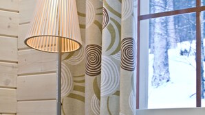 Een kamer met een houten wand, een vloerlamp, een raam met uitzicht op een besneeerd landschap en een bank met een oranje kussen.