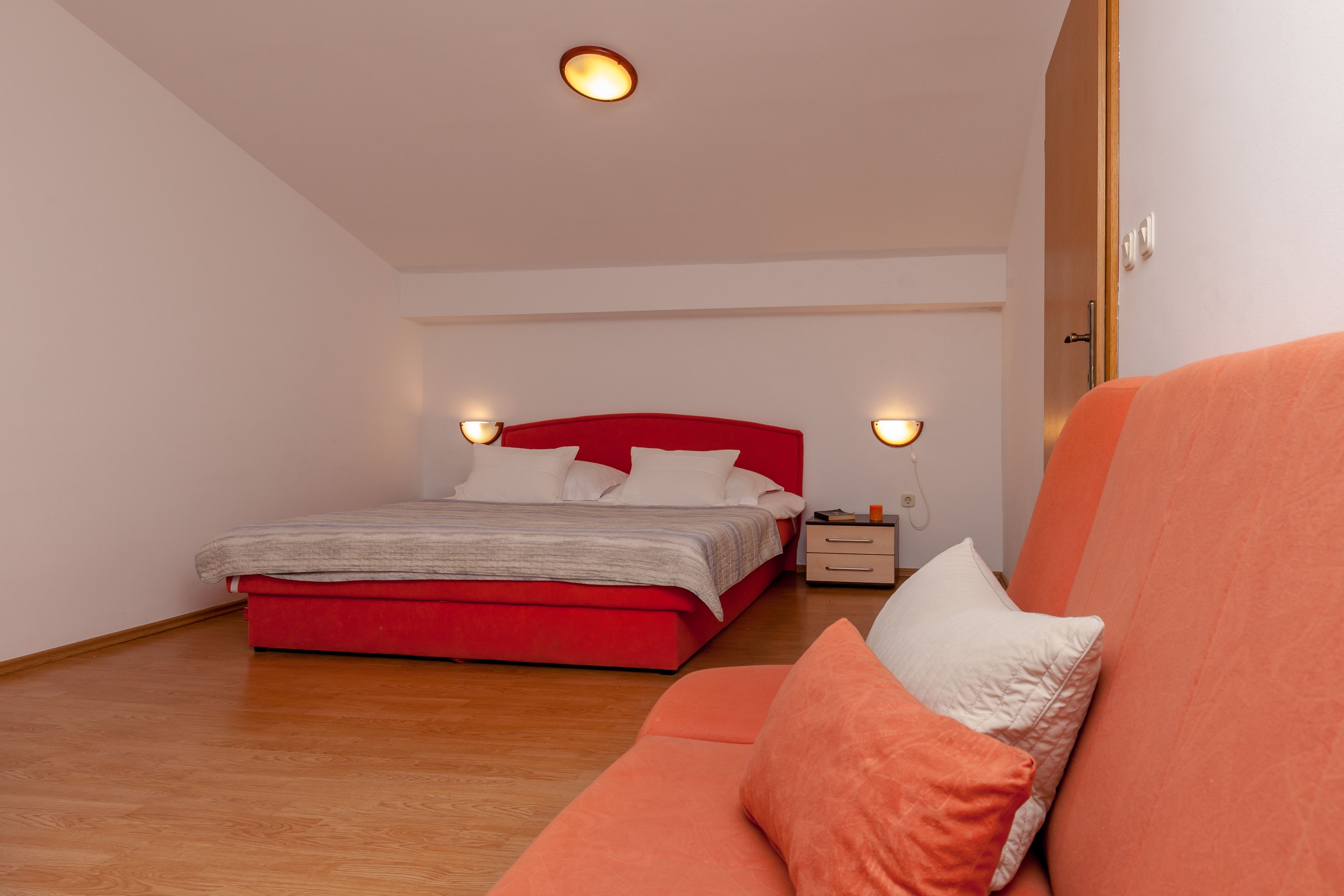 Ein Schlafzimmer mit einem roten Bett, Holzboden und einem roten und orangefarbenen Sofa.