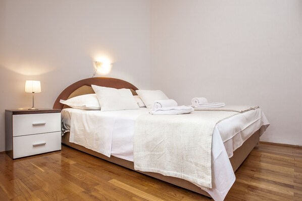A neatly made bed with white linens and a folded towel, a bedside lamp, and a wooden nightstand with drawers.