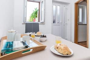 Un desayuno servido en una bandeja, con croissants, un libro y un bol de fruta sobre una mesa.