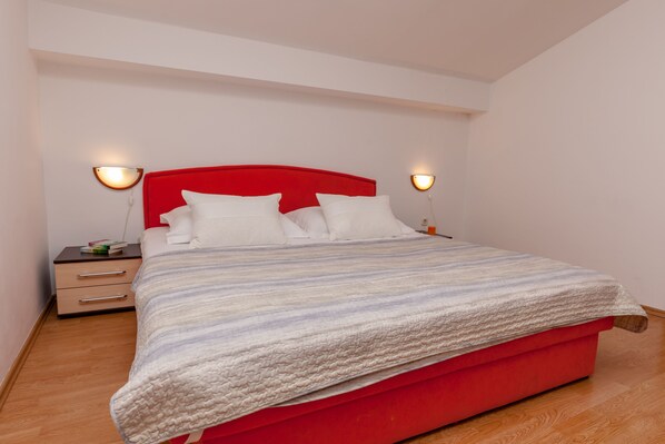 A modern bedroom with a red headboard, white bedding, and two bedside lamps.