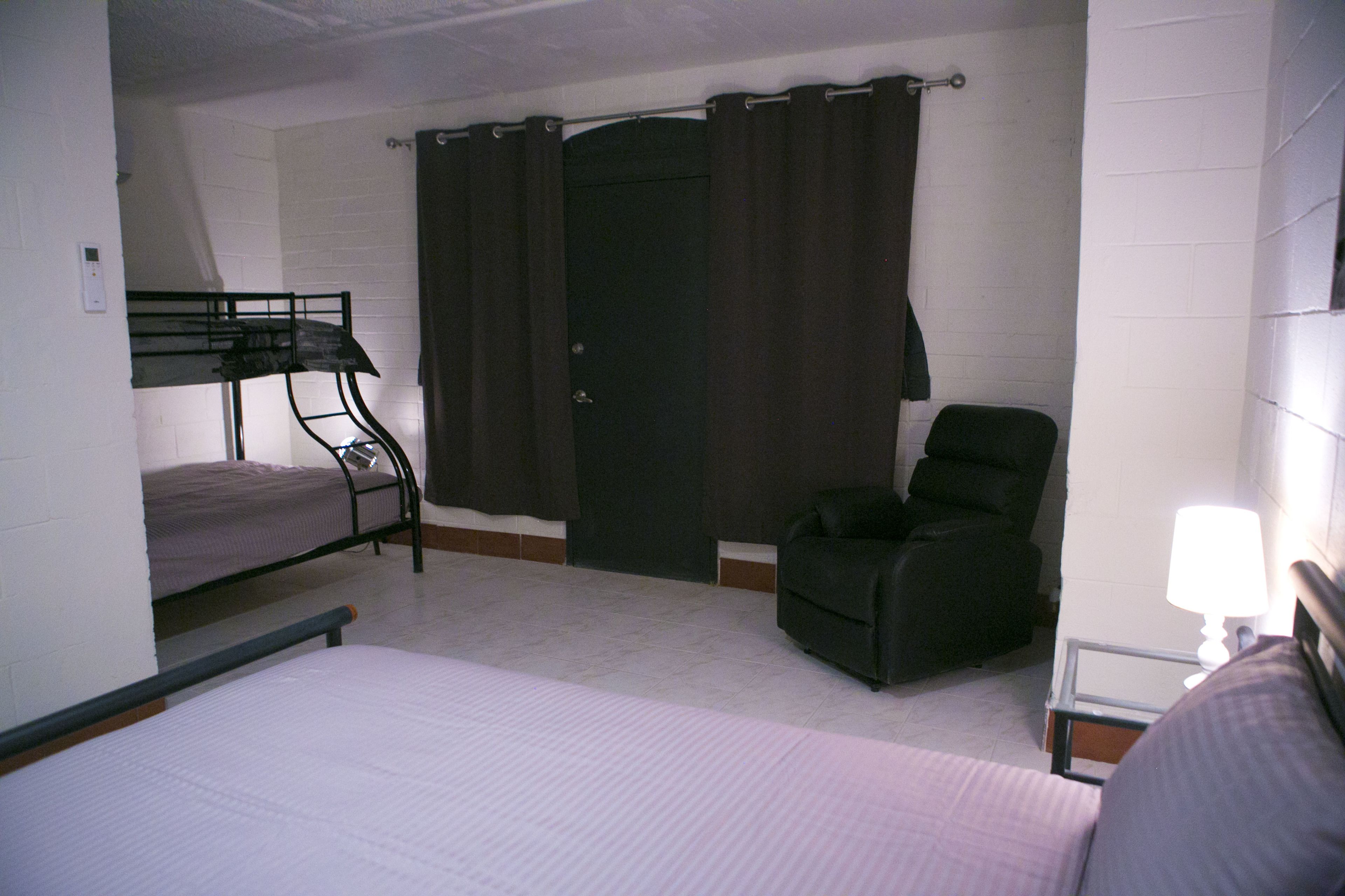 A room with a bunk bed, a chair, a desk with a lamp, and a door with curtains.