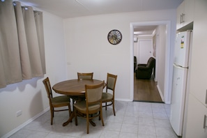 Un comedor con una mesa redonda de madera y cuatro sillas, un reloj de pared y un refrigerador.