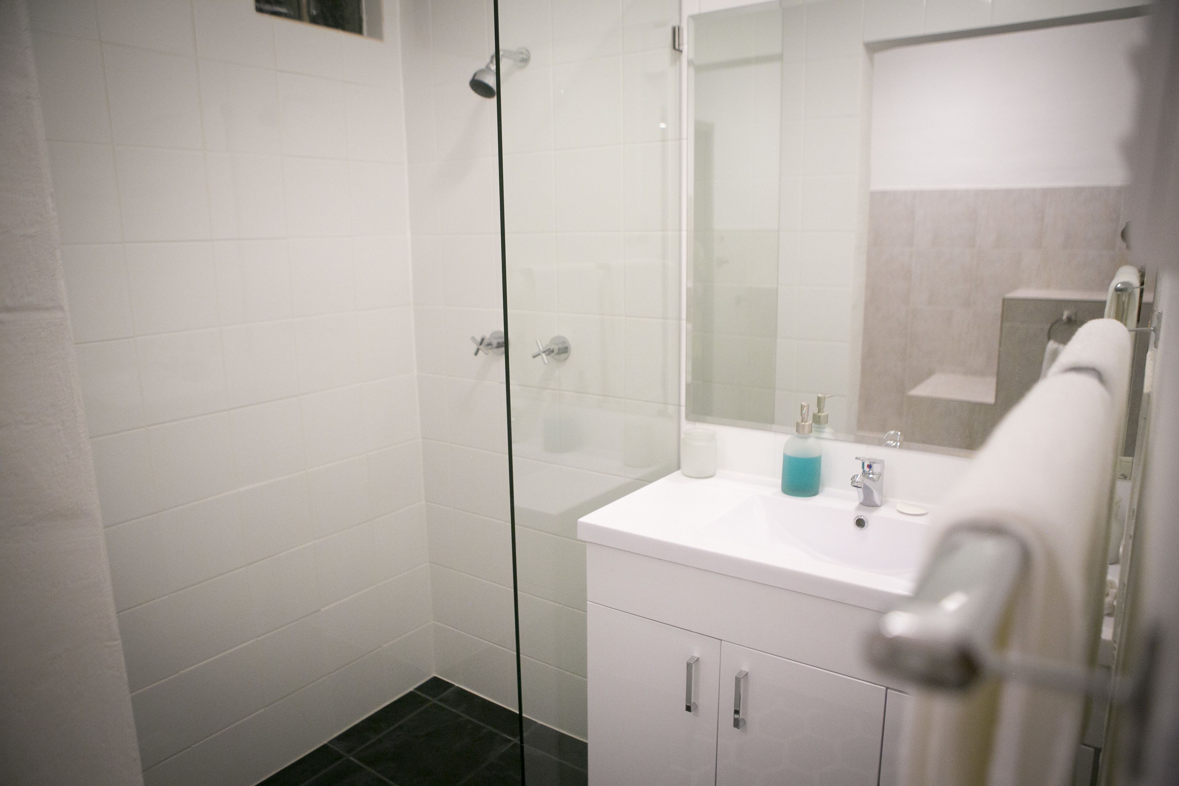 A modern bathroom with a glass shower enclosure, a white sink with a mirror, and a white cabinet.