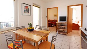 Un comedor con una mesa y sillas de madera, un frutero y un televisor al fondo.