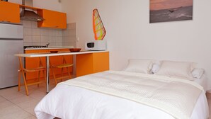 Un dormitorio con cama, escritorio y silla. Cuenta con una cocina equipada con estufa y microondas.