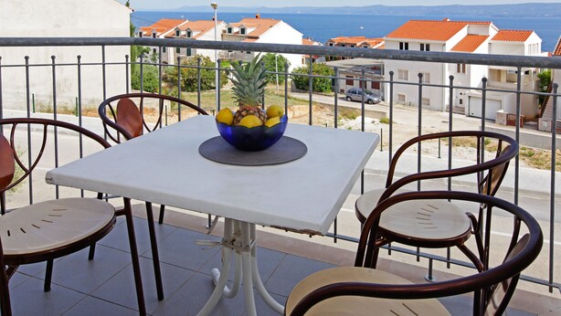 Un balcón con una mesa, sillas, un cuenco de fruta y vistas al mar y edificios.