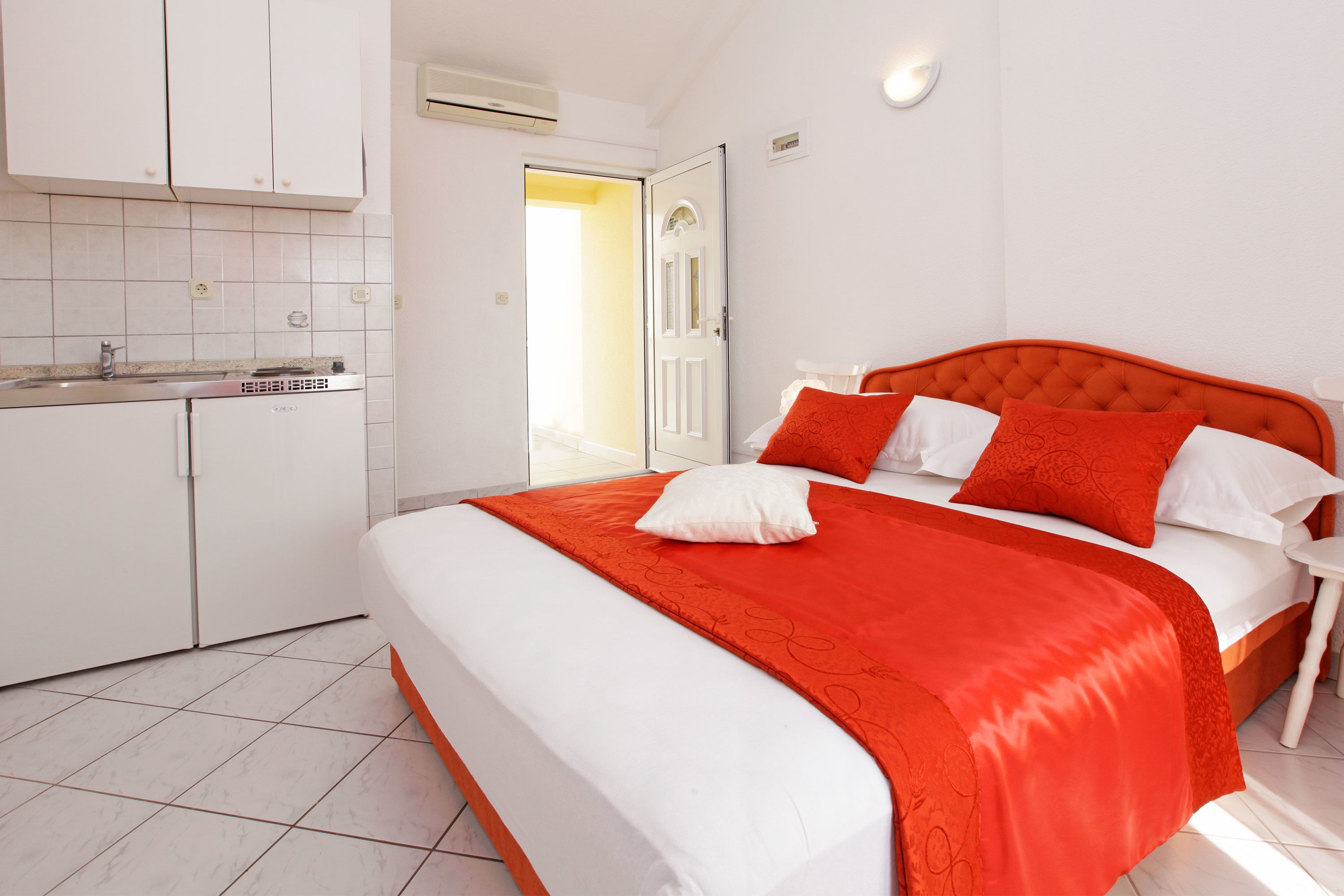 Une chambre à coucher avec un grand lit, une literie blanche et orange, une petite table de chevet et une armoire blanche.