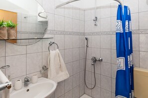 A bathroom with a sink, mirror, towel rack, shower, and blue shower curtain. - Ratac Apartments (Bol)