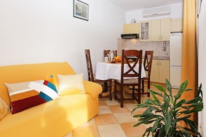 Un espai de viure compacte amb un sofà groc, una taula de dinar i una zona de cuina.