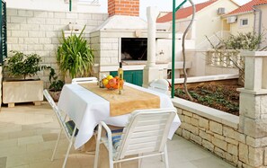 An outdoor patio with a table set for two, a brick oven, and potted plants. - Ratac Apartments (Bol)