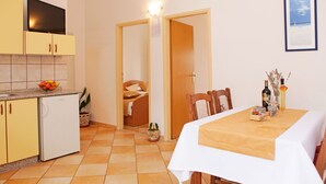 Et kompakt køkken med gule skabe, et hvidt køleskab og et spiseområde med et bord dækket til to.