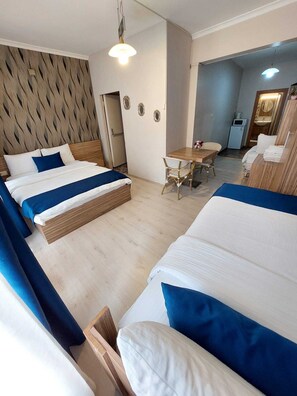 A hotel room with two beds, a dining table, and a small kitchenette.