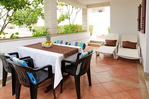 An outdoor patio with a table set for dining, surrounded by chairs with cushions. - Rose Garden Apartments (Bol)