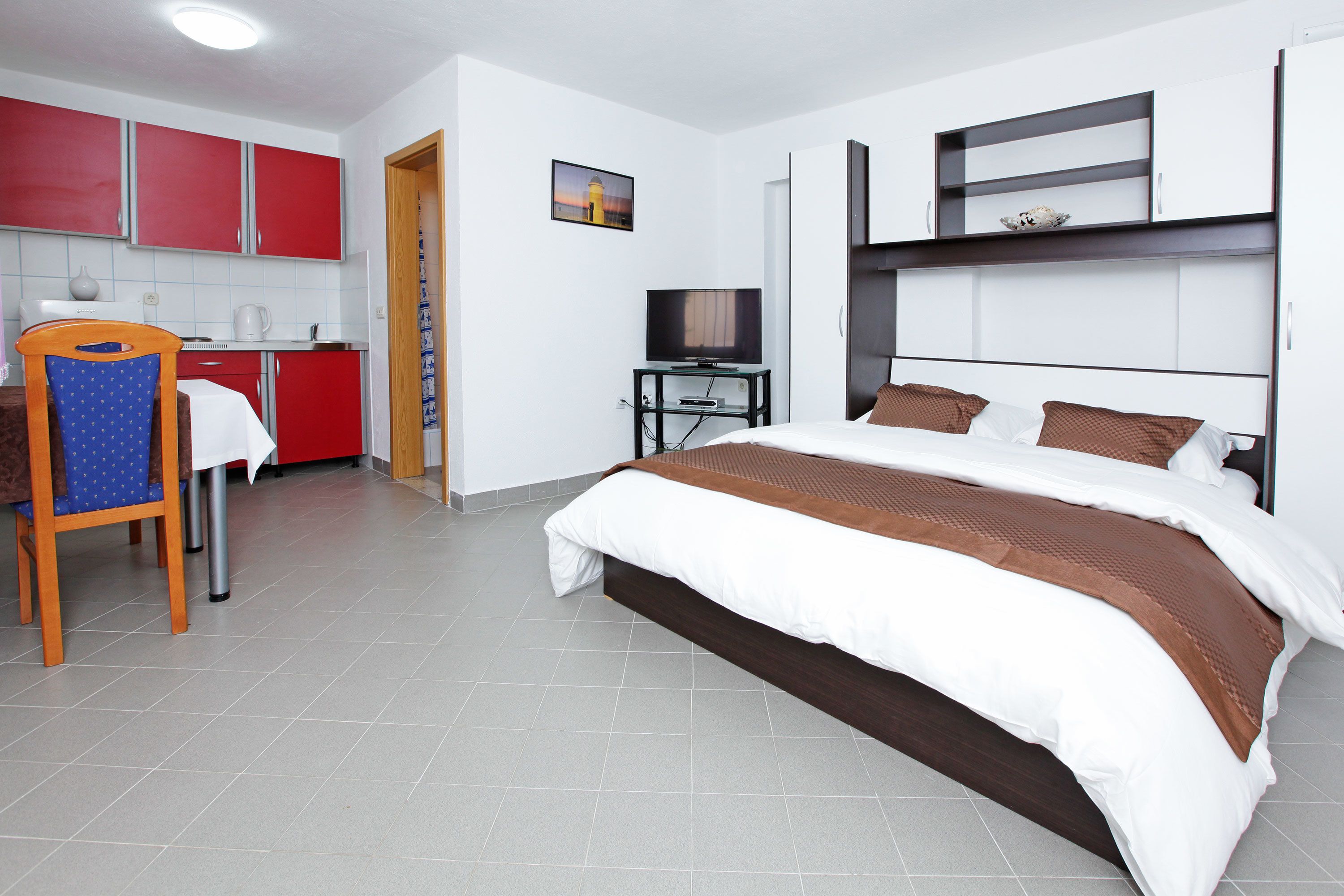 A hotel room with a bed, a TV, a desk, and a kitchenette.