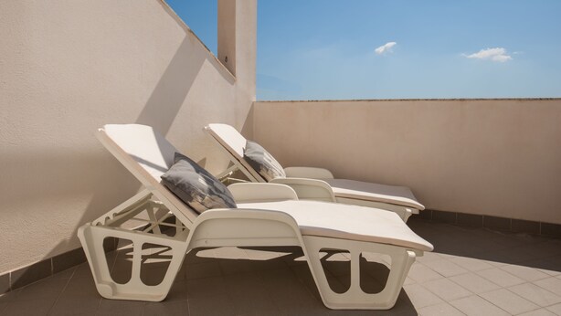 Una terraza en la azotea con tres tumbonas blancas, cada una con un cojín.