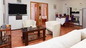 Sala de estar con sofá, una mesa de centro y un televisor sobre un mueble. Hay una zona de comedor con mesa y sillas.