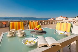 Una mesa con un cuenco de fruta, un libro y tazas en un balcón con vistas panorámicas.
