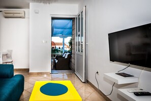A modern living room with a flat-screen TV, a sofa, a coffee table, and a balcony door. - Sunset Apartments (Bol)