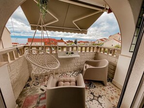 Un balcón con una silla colgante, dos sofás, una mesita y vistas al mar y edificios.