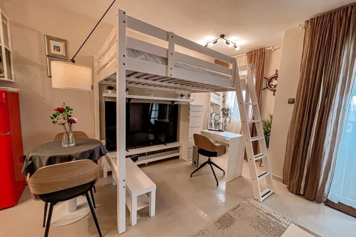 Ein Schlafzimmer mit Etagenbett, Schreibtisch, Stuhl, Fernseher und einem kleinen Tisch mit Blumen.