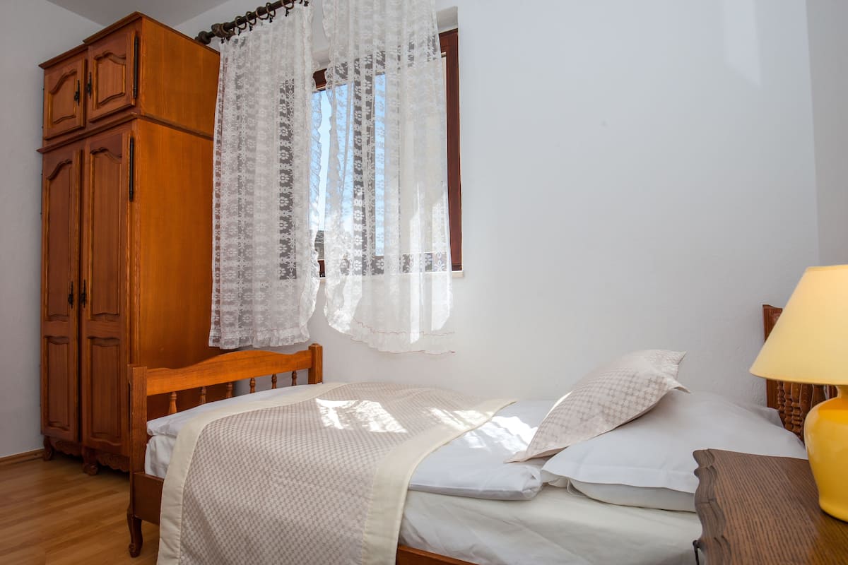Ein Schlafzimmer mit einem hölzernen Bett, weißer Bettwäsche, einem Holzschrank und einem Fenster mit transparenten Vorhängen.