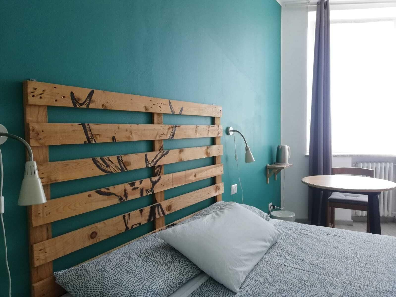 Une chambre avec un mur de couleur turquoise, une tête de lit en bois ornée de bois de cerf, un lit avec une literie à motifs, une lampe de chevet et une petite table sur laquelle se trouve une bouilloire.