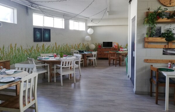 A spacious dining area with wooden tables and chairs, a television, and decorative plants.