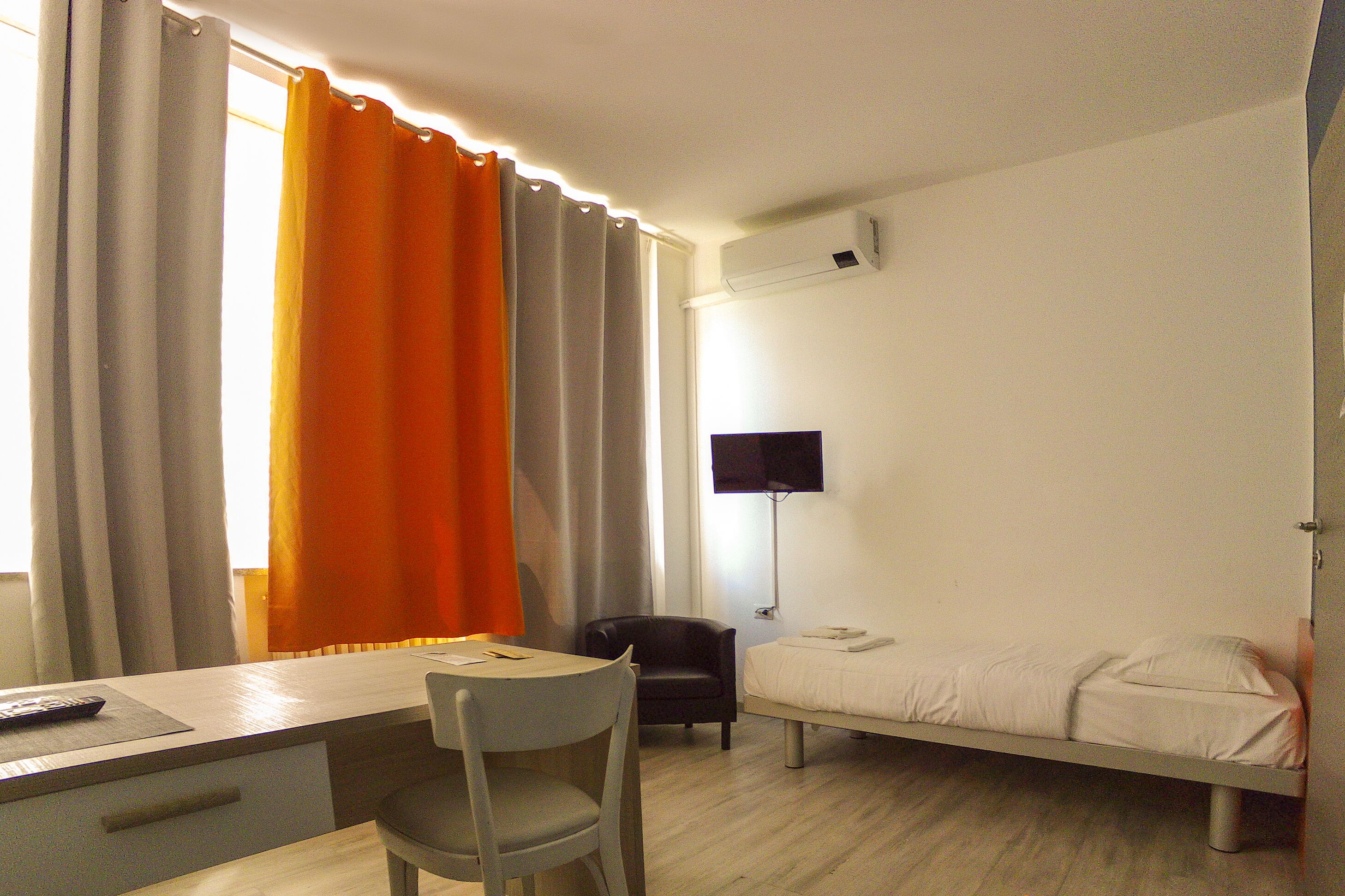 A bedroom with a bed, a desk, a chair, and a TV.