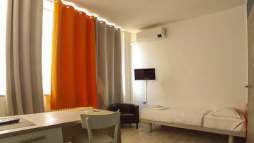 A bedroom with a bed, a desk, a chair, and a TV.