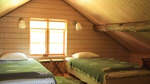 Une chambre mansardée accueillante, avec deux lits, une petite table et une fenêtre laissant entrer la lumière naturelle.