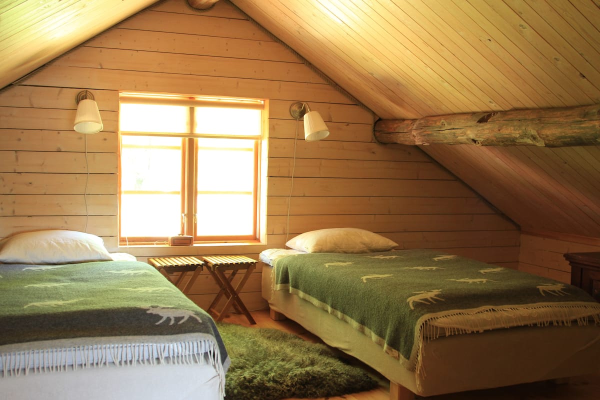 Une chambre mansardée accueillante, avec deux lits, une petite table et une fenêtre laissant entrer la lumière naturelle.